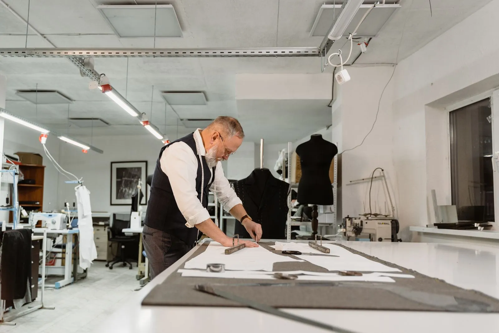 Male tailor meticulously crafting garment patterns at worktable in studio.